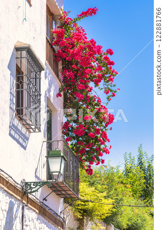 Granada town in Spain. Vibrant bougainvillea cascading down a white building's facade, creating a stunning display of color against the clear blue sky. Granada town in Spain. Vibrant bougainvillea cascading down a white building's facade, creating a stunning display of color against the clear blue sky. 122881766