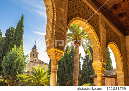Alhambra complex in Granada town, Andalusia, Spain. Ornate arches frame a sun-drenched courtyard, revealing palm trees and a distant tower. Alhambra complex in Granada town, Andalusia, Spain. Ornate arches frame a sun-drenched courtyard, revealing palm trees and a distant tower. 122881769