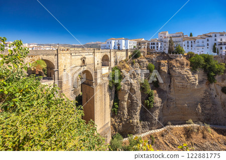 The Puente Nuevo bridge in El Tajo gorge in Ronda town in Spain. Ancient stone bridge spanning a deep gorge, with a white village perched on the cliffside. Sunny day, scenic view. 122881775