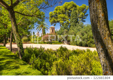 Alhambra complex in Granada town, Andalusia, Spain. Serene garden scene with ancient architecture peeking through lush greenery under a bright blue sky. Alhambra complex in Granada town, Andalusia, Spain. Serene garden scene with ancient architecture peeking through lush greenery under a bright blue sky. 122881804