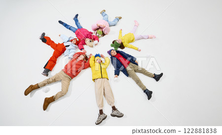 Children, girls and boys, dressed warm winter clothes lying on floor in circle, reaching out, laughing happily, creating playful winter atmosphere. 122881838