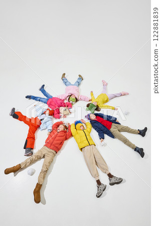 Group of children, girls and boys, dressed warm winter clothes lying in circle on floor, stretching arms with joy, laughing and enjoying winter fun. 122881839