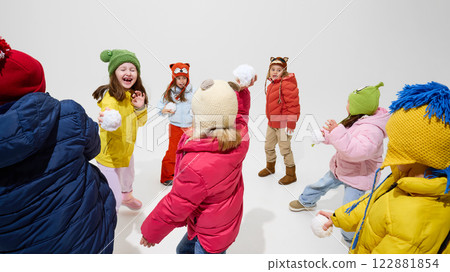 Group of children, laughing and playing, dressed warm winter outfits, throwing snowballs, having fun and energy-filled moment against white studio background. 122881854