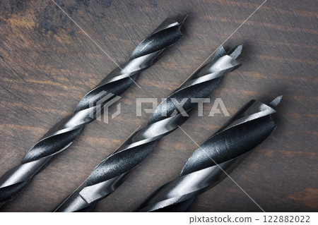 Close-up of three metal drill bits on a wooden surface. Close-up of three metal drill bits on a wooden surface. 122882022