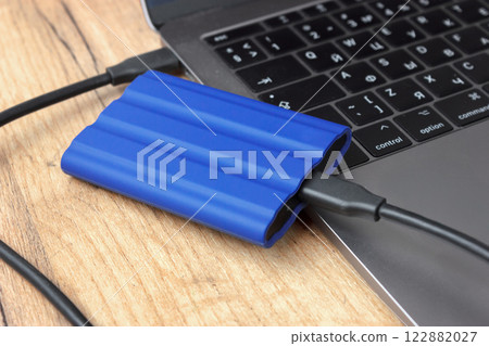 Blue external drive connected to a laptop on wooden desk. Blue external drive connected to a laptop on wooden desk. 122882027
