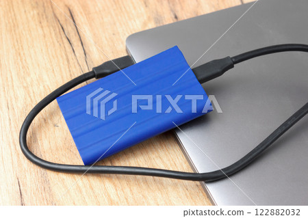 Blue external hard drive on a laptop, wood background. 122882032