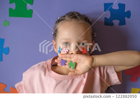 A child with details of multicolored puzzles in hand closes mouth, symbolizing silence. Problems of social perception of people with autism. A child with details of multicolored puzzles in hand closes mouth, symbolizing silence. Problems of social perception of people with autism. 122882050