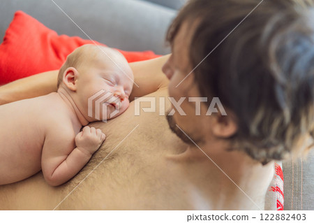 A newborn baby rests peacefully on the father's chest, feeling the warmth and heartbeat of his parent. A tender moment of bonding, love, and security, symbolizing the deep connection between father 122882403