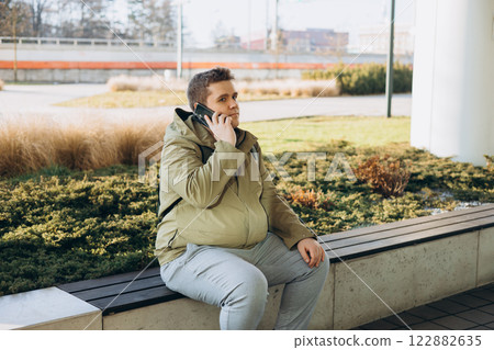 Business phone conversation. Happy blonde 30s man talking on smartphone on the city street. Communication and gadgets, connection concept. Man holding on cell smartphone while relaxing outdoors Business phone conversation. Happy blonde 30s man talking on smartphone on the city street. Communication and gadgets, connection concept. Man holding on cell smartphone while relaxing outdoors 122882635