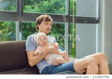 An exhausted father falls asleep on the couch while holding his 3-month-old baby in his arms. A tender and heartwarming moment showcasing love, caregiving, and the challenges of parenthood. Family and An exhausted father falls asleep on the couch while holding his 3-month-old baby in his arms. A tender and heartwarming moment showcasing love, caregiving, and the challenges of parenthood. Family and 122883792
