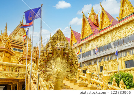Wat Kean Kleang golden buddhist pagoda temple walls, stairs and Naga snake statue in the foreground with cambodian flags waving on the wind, Phnom Penh, Cambodia 122883906
