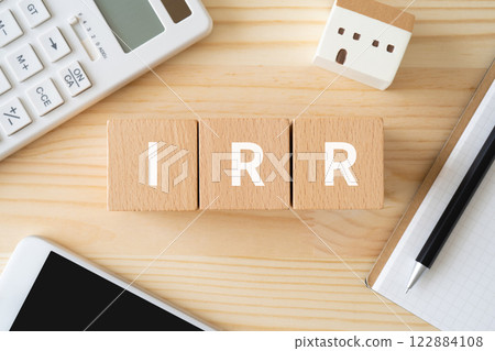 一塊寫著 IRR 的積木、一台計算器、一部智慧型手機和一棟模型建築 122884108