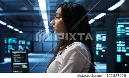 Programmer in data center typing on computer keyboard, ensuring system can handle networking tasks. IT specialist in server farm tracking network traffic with PC, camera B 122885026