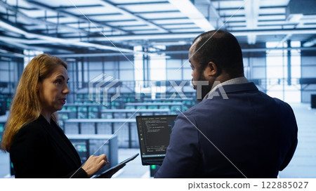 Teamworking coworkers doing maintenance using devices, prolonging data center hardware life span. Colleagues doing brainstorming in server hub, monitoring server infrastructure using devices, camera A 122885027