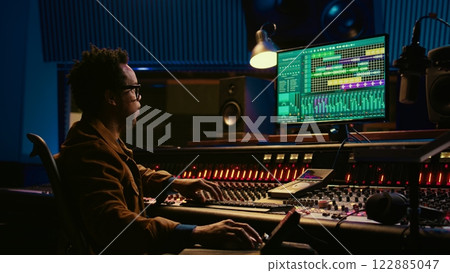 African american sound designer working with editing software to produce new tracks. Audio engineer uses mixer and compressor, changes volume level and sound settings in post production. Camera B. African american sound designer working with editing software to produce new tracks. Audio engineer uses mixer and compressor, changes volume level and sound settings in post production. Camera B. 122885047
