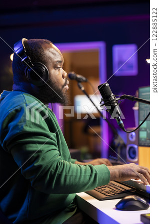 Skilled composer producing a new melody with lyrics and piano keys, recording audio files to edit them with mixing console. Young talented artist producer creating soundtracks. Skilled composer producing a new melody with lyrics and piano keys, recording audio files to edit them with mixing console. Young talented artist producer creating soundtracks. 122885122