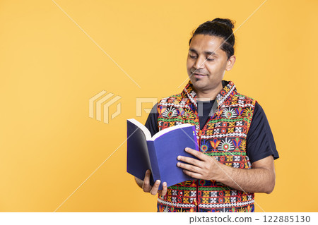 Indian man reading book, having fun and enjoying characters and plot, isolated over studio background. Relaxed person browsing novel, enjoying leisure time, appreciating literature 122885130