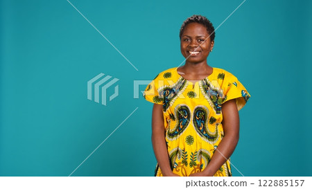 Portrait of cute stylish girl smiling and holding arms crossed in studio, wearing a native floral pattern outfit to ensemble african ethnic clothing. Young woman natural beauty. Camera B. Portrait of cute stylish girl smiling and holding arms crossed in studio, wearing a native floral pattern outfit to ensemble african ethnic clothing. Young woman natural beauty. Camera B. 122885157