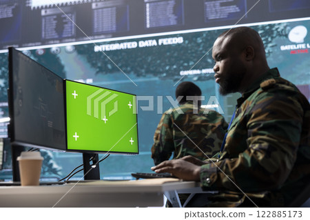 Military expert handles satellite cctv data next to mockup screen, working in a base of operations with high tech gear to support important defense missions. Coordinates strategic tactics. Military expert handles satellite cctv data next to mockup screen, working in a base of operations with high tech gear to support important defense missions. Coordinates strategic tactics. 122885173