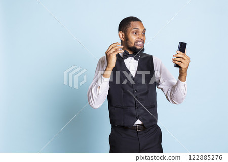 Hotel concierge chatting with guests on videoconference call with phone, discussing with clients about amenities. Bellhop doorman on online videocall connection, professionalism. 122885276