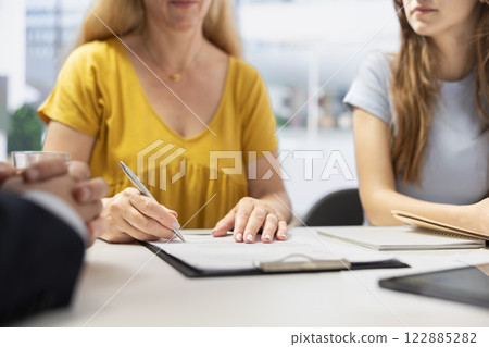 Clients completing forms, taking loan from financial agent, doing handshake after completing deal. Mother and daughter signing contract, entering agreement with financial consultant, close up shot 122885282