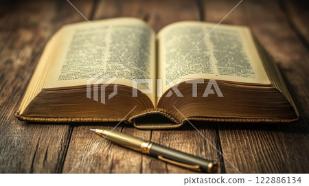 A book is open on a wooden table with a pen on the table 122886134
