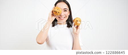 Close up portrait of smiling korean woman, shows tasty cupcakes, eating cake and looking happy, pastry and bakery concept 122886645
