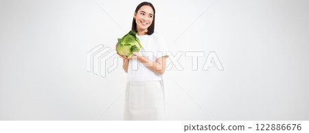 Waist up portrait of smiling asian woman, holding cabbage, recommends eating vegetables, healthy organic green food, isolated on white background 122886676