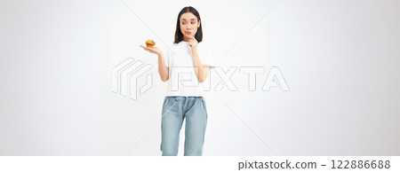 Portrait of asian girl with pensive face, holds cupcake with thinking face, isolated on white background 122886688