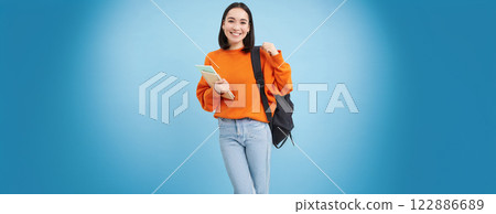 Education and students. Smiling young asian woman with backpack and notebooks, posing against blue background Education and students. Smiling young asian woman with backpack and notebooks, posing against blue background 122886689