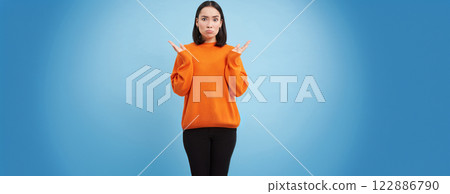 Asian girl with confused face, shrugs shoulders and pouts, looks upset and clueless, dont understand, puzzled by smth, stands over blue background Asian girl with confused face, shrugs shoulders and pouts, looks upset and clueless, dont understand, puzzled by smth, stands over blue background 122886790