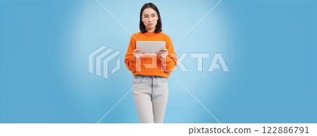 Woman with digital tablet thinking, looking aside with thoughtful face expression, standing over blue background Woman with digital tablet thinking, looking aside with thoughtful face expression, standing over blue background 122886791