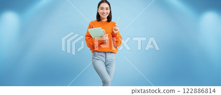 Education and students. Happy asian woman, holding notebooks and laughing, smiling at camera, enjoys going to University or College, blue background Education and students. Happy asian woman, holding notebooks and laughing, smiling at camera, enjoys going to University or College, blue background 122886814