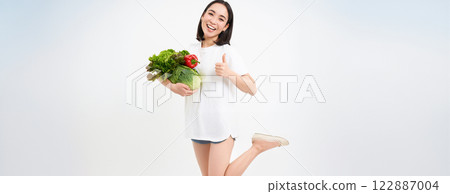 Smiling happy asian woman shows thumbs up and vegetables, eating healthy raw food, isolated over white background 122887004