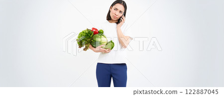 Image of girl with vegetables, making phone call with sad, unhappy face, isolated on white background 122887045