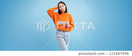 Woman with digital tablet, looks confused, cant understand smth on her gadget, stands puzzled against blue background 122887046