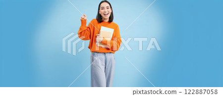 Education and students. Happy asian woman, holding notebooks and laughing, smiling at camera, enjoys going to University or College, blue background 122887058