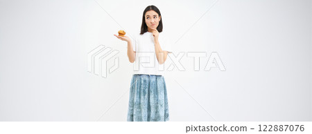 Woman with pensive face, holding cupcake and thinking, white background Woman with pensive face, holding cupcake and thinking, white background 122887076