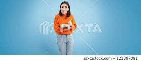Education and students. Happy asian woman, holding notebooks and laughing, smiling at camera, enjoys going to University or College, blue background 122887081