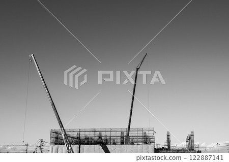 Crane and building construction scaffolding stretching out against the blue sky, monochrome 122887141