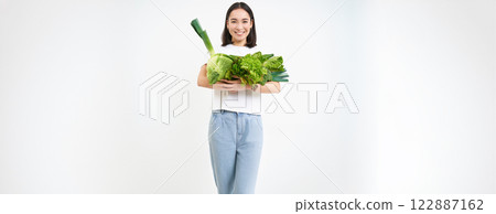 Image of smiling asian woman, vegetarian with lots of green vegetables, eating oranic food, isolated on white background Image of smiling asian woman, vegetarian with lots of green vegetables, eating oranic food, isolated on white background 122887162
