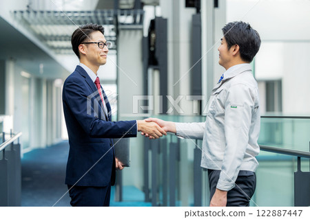 握手:一個穿工作服的男人和一個穿西裝的男人 握手:一個穿工作服的男人和一個穿西裝的男人 122887447
