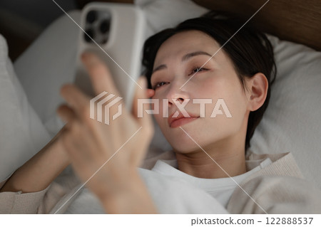 一名婦女在床上的看一個智能手機 一名婦女在床上的看一個智能手機 122888537