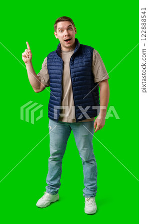 Man in a navy vest gestures enthusiastically toward a green screen Man in a navy vest gestures enthusiastically toward a green screen 122888541