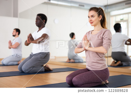 Woman kneeling on mat during group yoga training Woman kneeling on mat during group yoga training 122889828