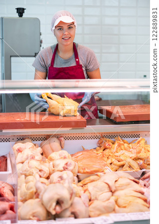 Young female butcher showing fresh raw farm chickens Young female butcher showing fresh raw farm chickens 122889831