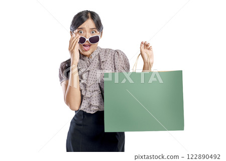 Portrait of an Asian Indonesian woman with sunglasses carrying a shopping bag isolated over a white background. Copy space or mockup. Concept of shopping, lifestyle, or consumerism 122890492