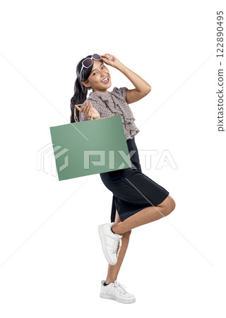 Portrait of an Asian Indonesian woman with sunglasses carrying a shopping bag isolated over a white background. Copy space or mockup. Concept of shopping, lifestyle, or consumerism 122890495