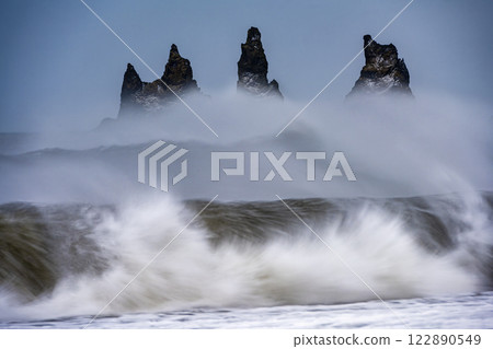 Panoramic view of ocean waves with protruding rocks from black sand beach Reynisfjara, Iceland. Nature, travel, winter background, or wallpaper Panoramic view of ocean waves with protruding rocks from black sand beach Reynisfjara, Iceland. Nature, travel, winter background, or wallpaper 122890549