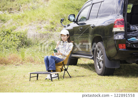 一位年輕女子獨自坐在汽車露營地的椅子上放鬆 122891558
